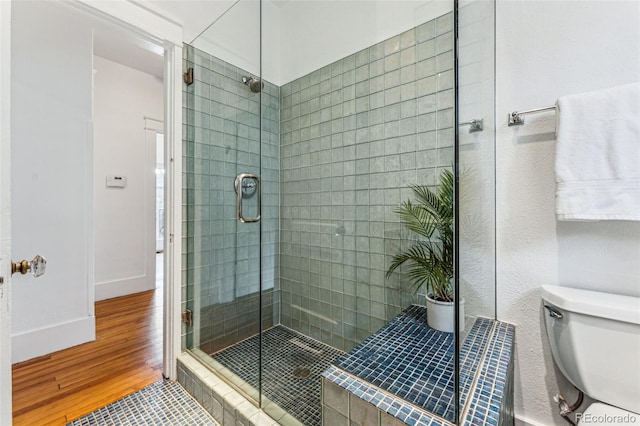 bathroom featuring toilet, a shower stall, baseboards, and wood finished floors