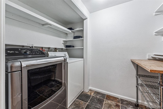 washroom with a textured wall, laundry area, baseboards, stone finish floor, and washing machine and clothes dryer