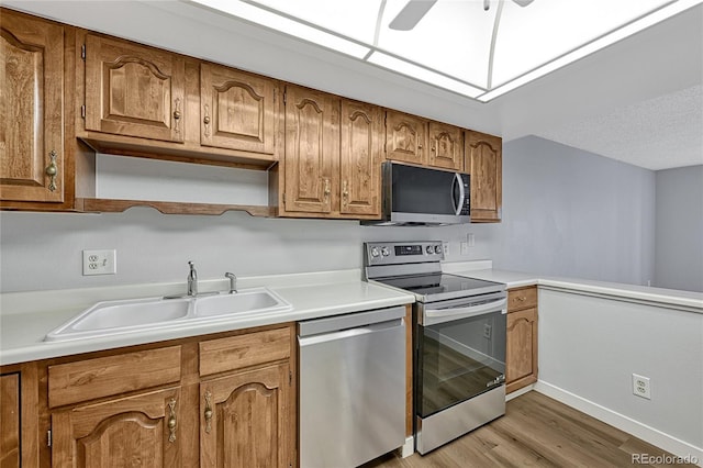 kitchen featuring light countertops, light wood-type flooring, brown cabinets, appliances with stainless steel finishes, and a sink