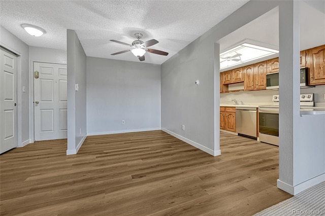 unfurnished living room with ceiling fan, a textured ceiling, baseboards, and wood finished floors