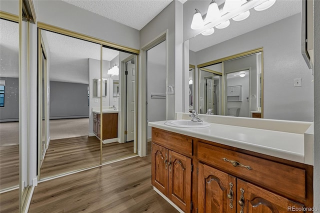 full bath featuring vanity, wood finished floors, a baseboard radiator, and a textured ceiling