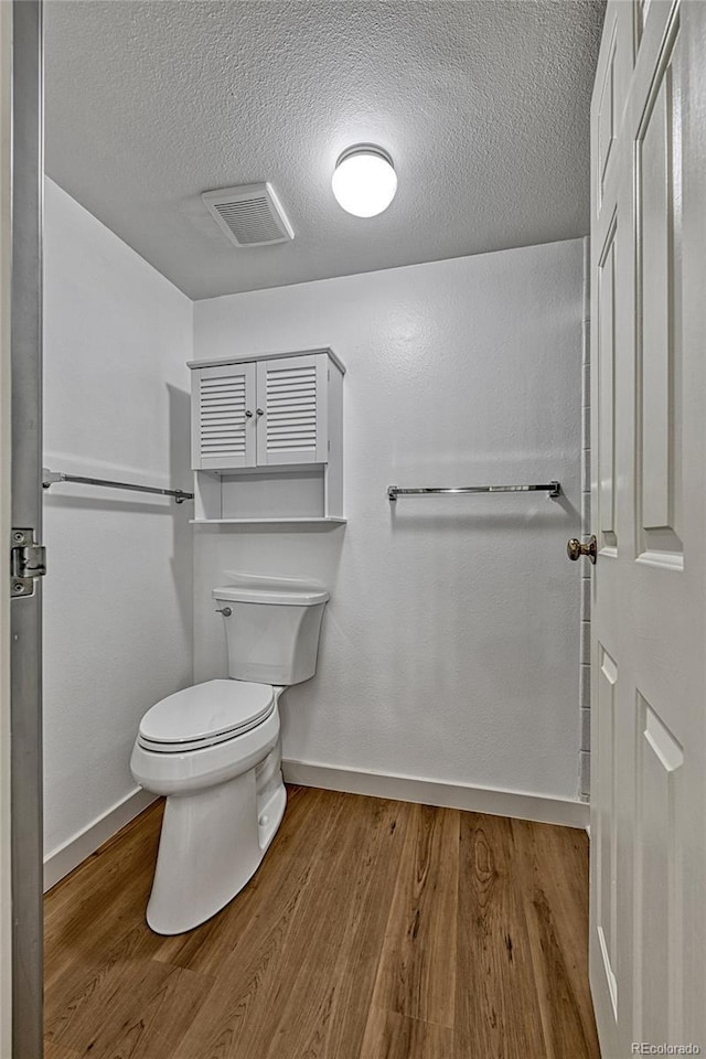 bathroom featuring toilet, wood finished floors, visible vents, and a textured ceiling