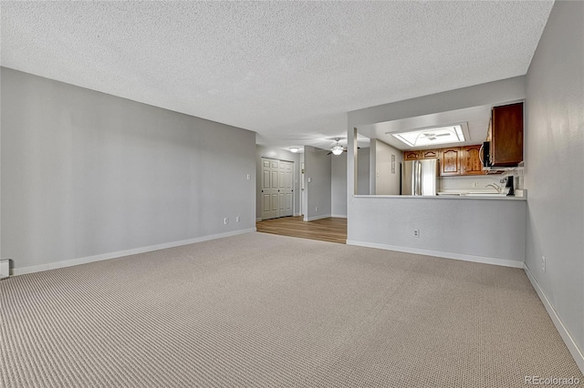 unfurnished living room featuring light colored carpet, a textured ceiling, baseboards, and ceiling fan