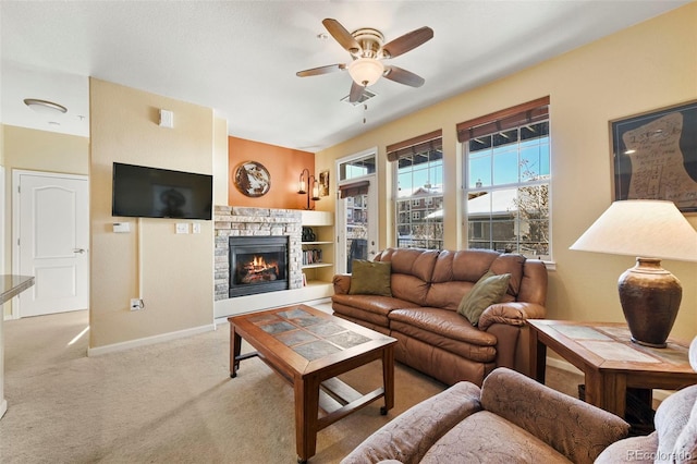 carpeted living room featuring a stone fireplace and ceiling fan