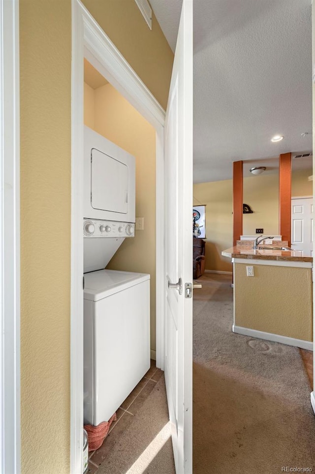 laundry room featuring a textured ceiling, sink, light colored carpet, and stacked washer / dryer