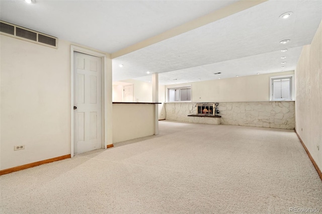 below grade area featuring visible vents, baseboards, a warm lit fireplace, carpet flooring, and recessed lighting
