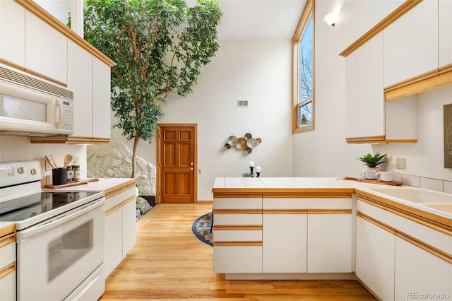 kitchen featuring light wood-style floors, a peninsula, a healthy amount of sunlight, and white appliances