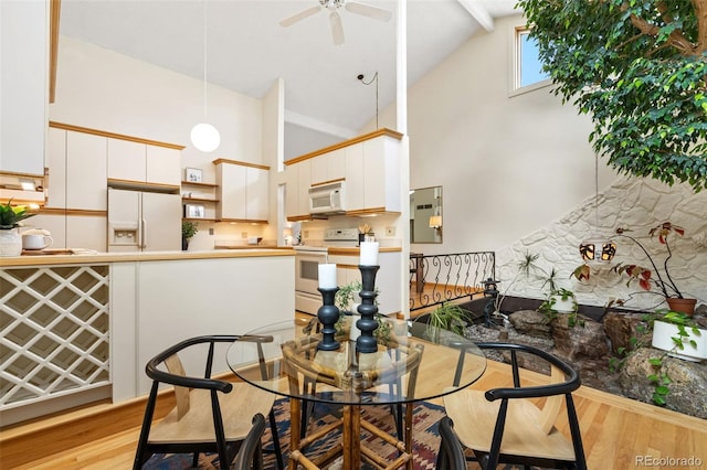 dining area with high vaulted ceiling, ceiling fan, and light wood-style flooring