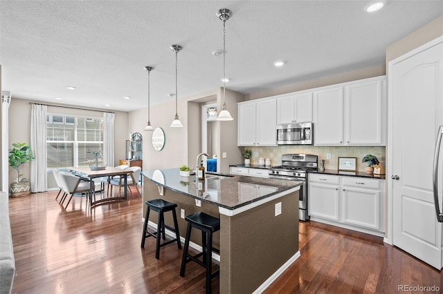 827 Sundance Ln, Erie, CO 80516 - kitchen with a sink, hanging light fixtures, a kitchen island with sink, appliances with stainless steel finishes, and dark wood-type flooring