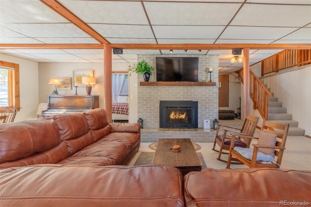 carpeted living room with a brick fireplace, a drop ceiling, and stairway