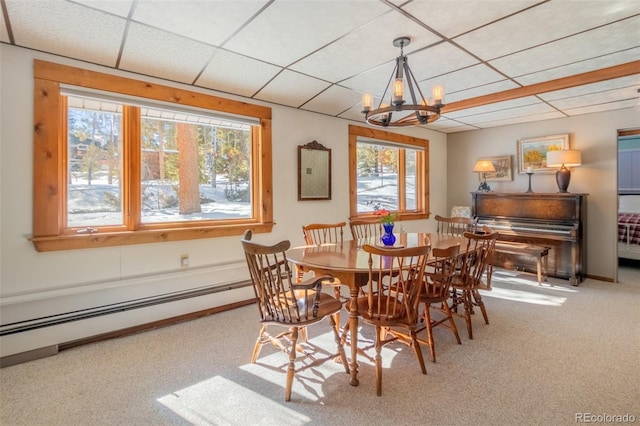 carpeted dining area with a paneled ceiling, baseboards, a baseboard heating unit, and a notable chandelier