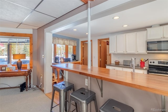 kitchen featuring stainless steel appliances, a breakfast bar, white cabinetry, and wooden counters