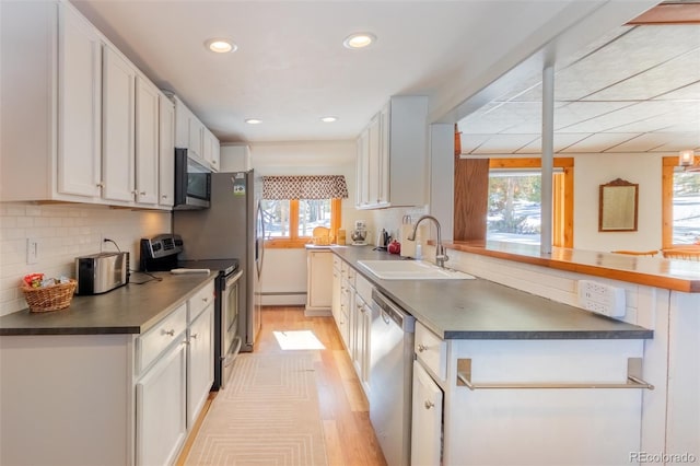 kitchen with white cabinets, dark countertops, a peninsula, stainless steel appliances, and a sink