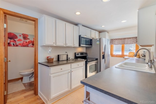 kitchen featuring tasteful backsplash, dark countertops, stainless steel appliances, white cabinetry, and a sink