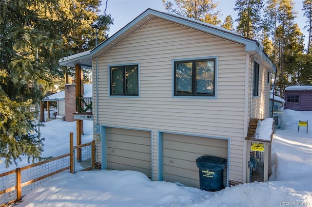 view of snow covered exterior with a garage and fence