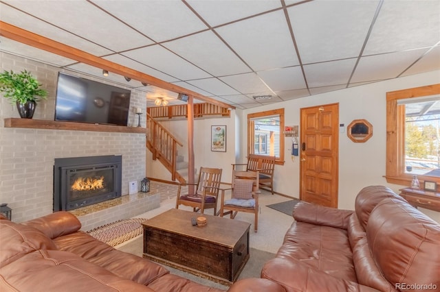 carpeted living room featuring a paneled ceiling, a brick fireplace, and stairs