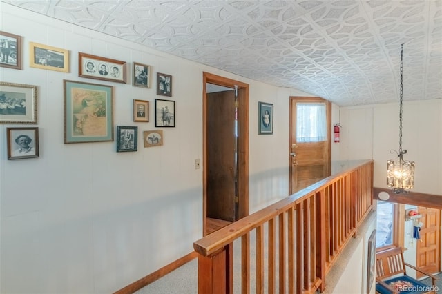 hallway with an ornate ceiling, lofted ceiling, an inviting chandelier, an upstairs landing, and baseboards