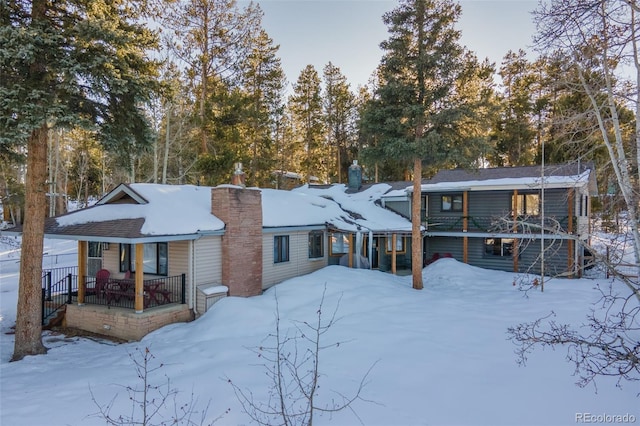 snow covered rear of property with a chimney and a porch