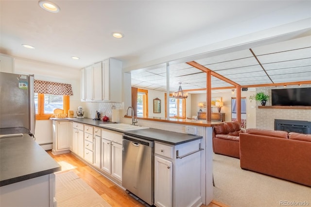 kitchen featuring a baseboard radiator, a peninsula, a sink, appliances with stainless steel finishes, and dark countertops