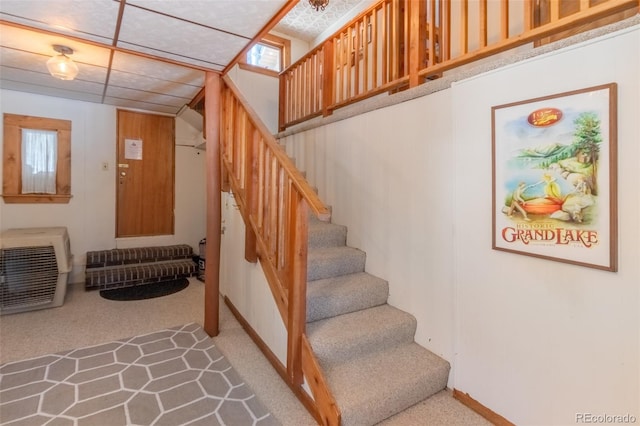 staircase with a paneled ceiling, carpet flooring, and baseboards