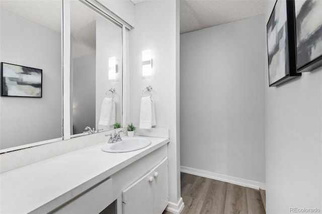 bathroom with a textured ceiling, wood finished floors, vanity, and baseboards