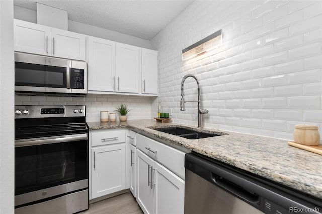 kitchen with tasteful backsplash, stainless steel appliances, a textured ceiling, white cabinetry, and a sink