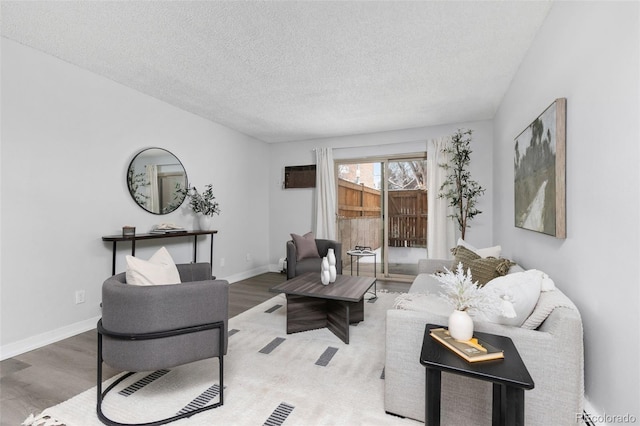 living area with a wall mounted AC, a textured ceiling, baseboards, and wood finished floors