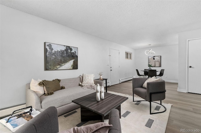 living room with a textured ceiling, baseboard heating, light wood-type flooring, and visible vents