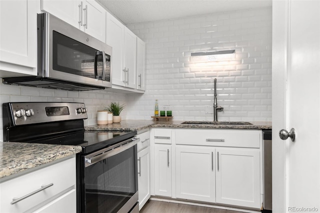 kitchen featuring appliances with stainless steel finishes, white cabinetry, a sink, and tasteful backsplash