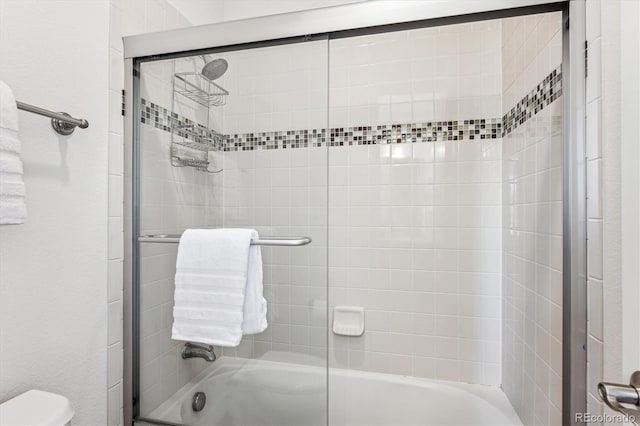 bathroom featuring toilet and bath / shower combo with glass door