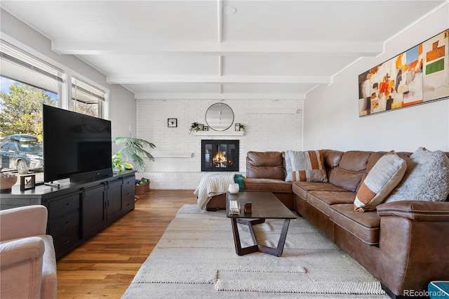 living room featuring beamed ceiling, brick wall, a fireplace, and hardwood / wood-style flooring