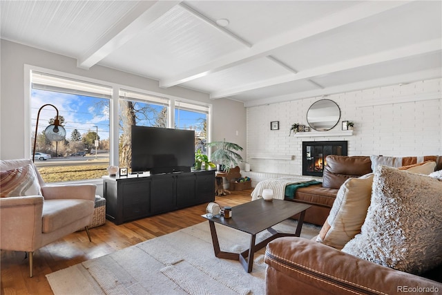 living room featuring a brick fireplace, beam ceiling, wood-type flooring, and brick wall