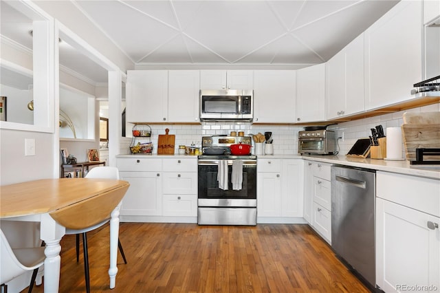 kitchen with crown molding, white cabinetry, backsplash, hardwood / wood-style floors, and stainless steel appliances