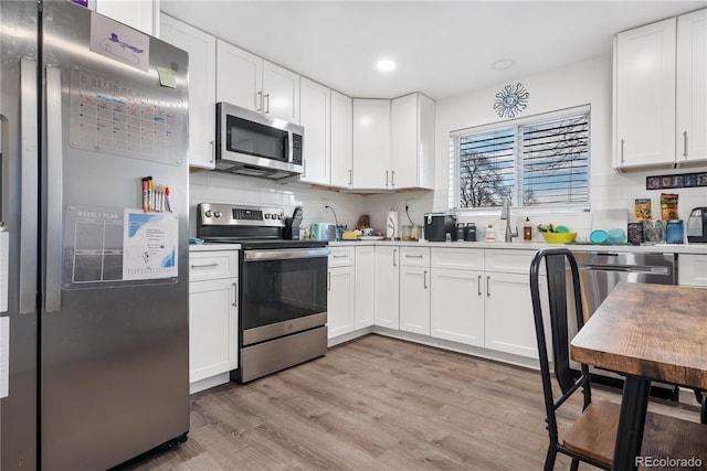 kitchen with white cabinetry, appliances with stainless steel finishes, backsplash, and light wood-type flooring