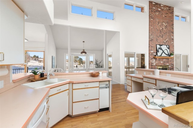 kitchen featuring pendant lighting, sink, dishwashing machine, white cabinets, and light hardwood / wood-style flooring