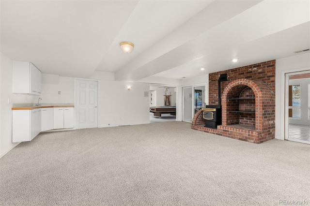 unfurnished living room featuring sink, light colored carpet, and a wood stove