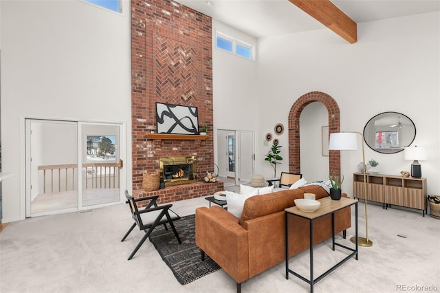 carpeted living room with a towering ceiling, beam ceiling, and a brick fireplace