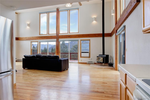 living room featuring a wood stove, light wood-type flooring, a high ceiling, and a baseboard radiator