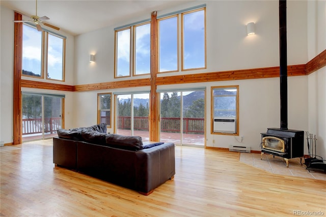 living room featuring ceiling fan, a wood stove, light hardwood / wood-style flooring, and a towering ceiling