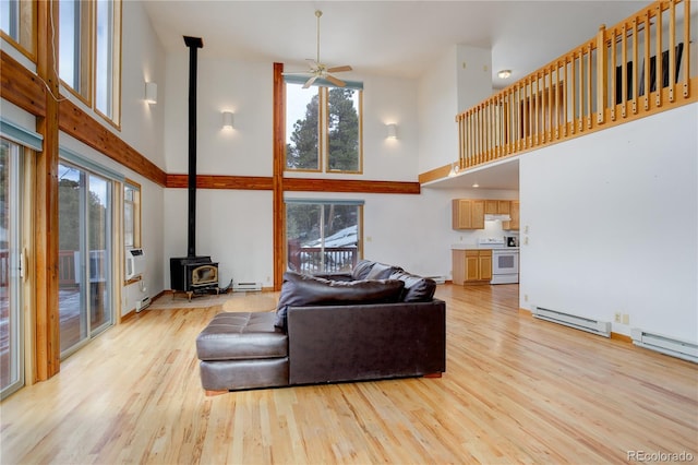 living room with a wood stove, light hardwood / wood-style floors, a high ceiling, and a wealth of natural light