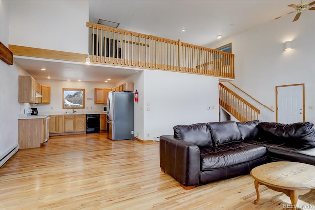 living room with ceiling fan, sink, light wood-type flooring, and a high ceiling