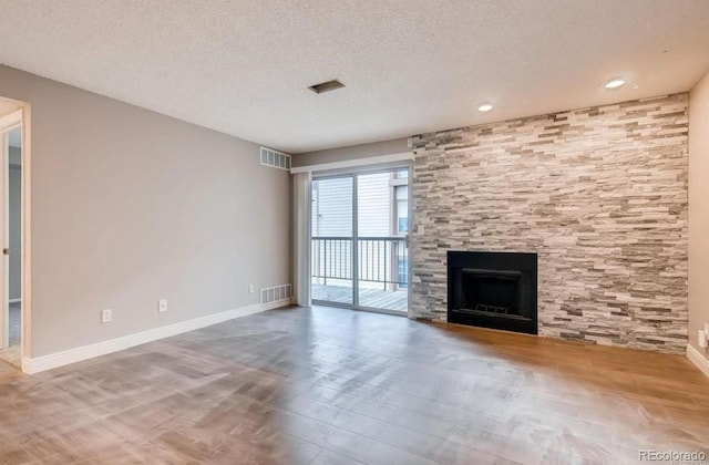 unfurnished living room with a textured ceiling, hardwood / wood-style flooring, and a stone fireplace