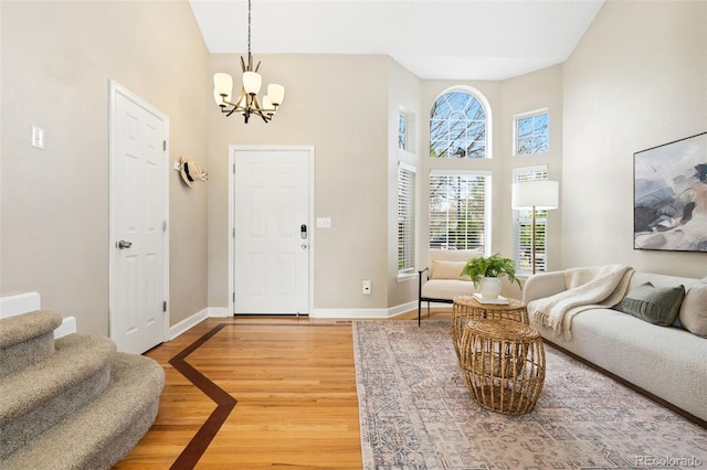 interior space featuring a towering ceiling, stairway, baseboards, a notable chandelier, and light wood-style flooring