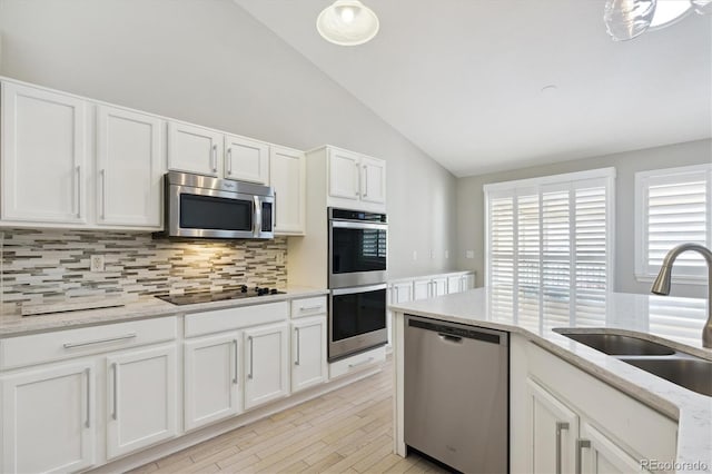 kitchen featuring lofted ceiling, appliances with stainless steel finishes, white cabinetry, light hardwood / wood-style flooring, and sink