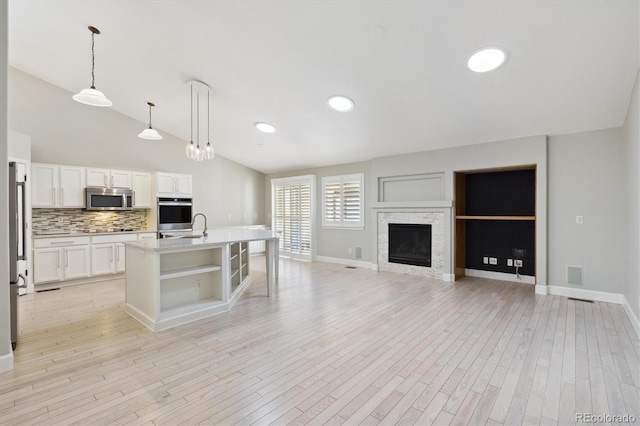 kitchen with a kitchen island with sink, vaulted ceiling, decorative light fixtures, appliances with stainless steel finishes, and light hardwood / wood-style floors