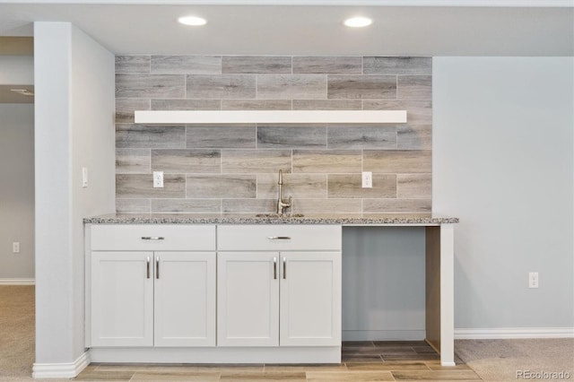 bar featuring white cabinetry, light hardwood / wood-style floors, light stone countertops, and sink