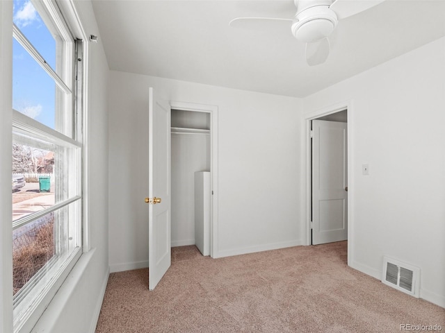 unfurnished bedroom with baseboards, visible vents, light colored carpet, ceiling fan, and a closet