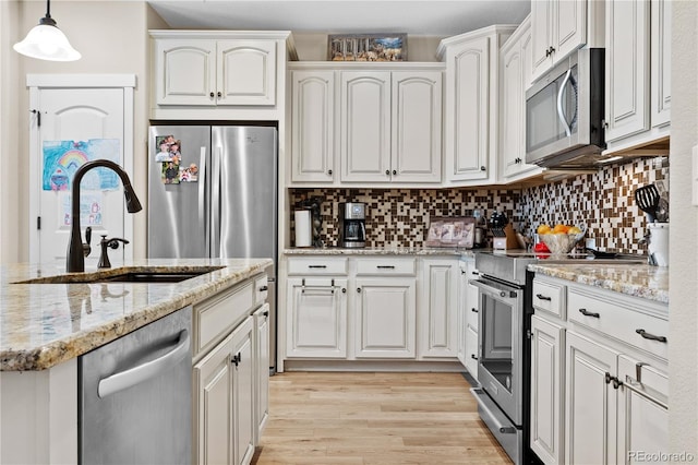 kitchen with appliances with stainless steel finishes, decorative light fixtures, white cabinetry, sink, and backsplash