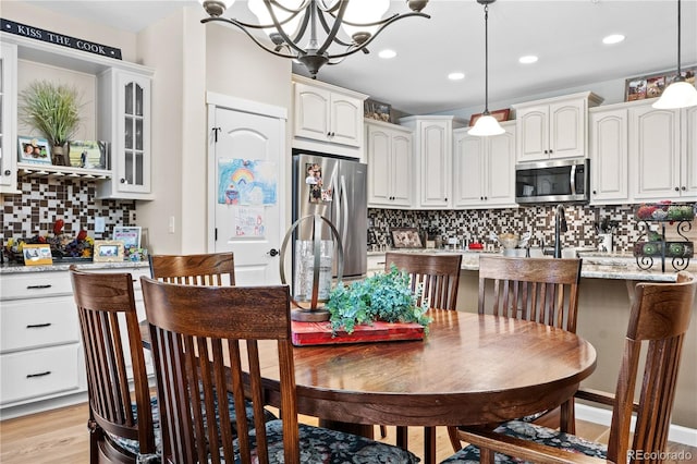 kitchen with tasteful backsplash, hanging light fixtures, light wood-type flooring, stainless steel appliances, and white cabinets