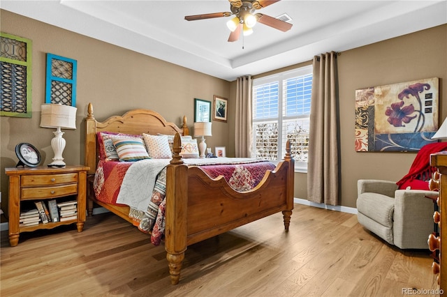 bedroom with ceiling fan, a tray ceiling, and light hardwood / wood-style flooring